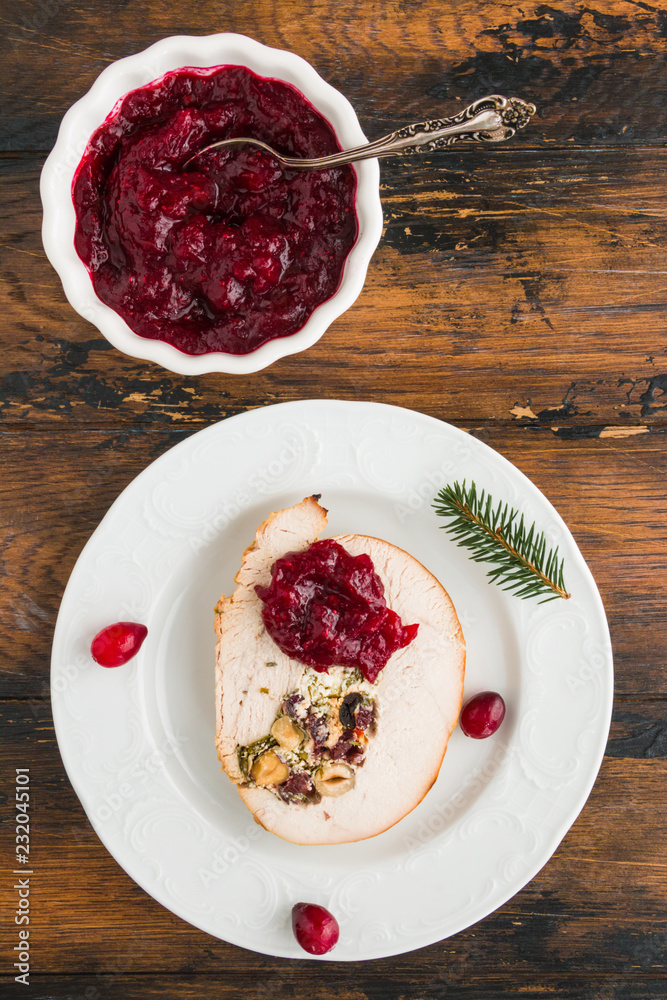 Stuffed turkey breast roll with cranberry sauce on white plate on rustic wooden table, top view Stuffed turkey breast roll with cranberry sauce on white plate on rustic wooden table, top view