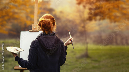 girl drawing a picture on an easel in nature, young woman with paint brush among autumn trees, a concept of creativity and a hobby