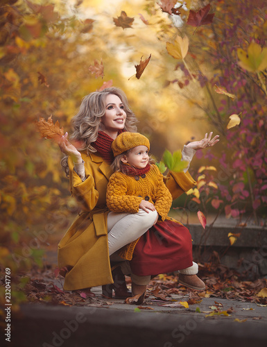 Happy mother and daughter in the autumn forest throw leaves and laugh. Family in clothes autumn flowers walk in the autumn Park.