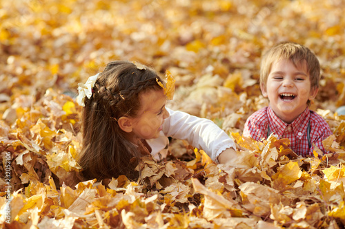 Children are lying and palying in fallen leaves in autumn city park.