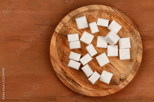 An overhead photo of sugar cubes on a wooden plate, shot from above on a dark rustic wooden background with copy space
