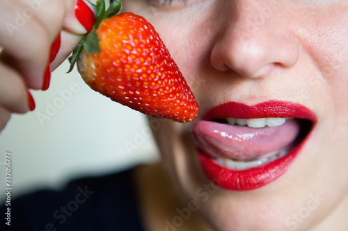 The girl sexually licks the strawberry berry with her tongue.