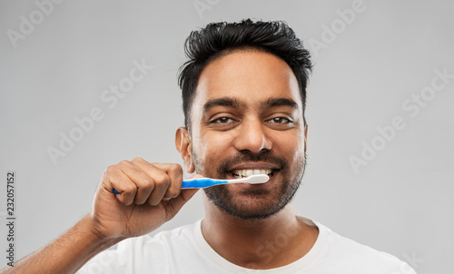 oral care, dental hygiene and people concept - smiling young indian man with toothbrush cleaning teeth over gray background