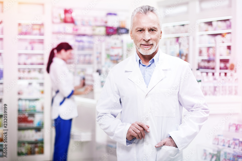 Confident grey-haired pharmacist holding his hand in the pocket Confident grey-haired pharmacist holding his hand in the pocket