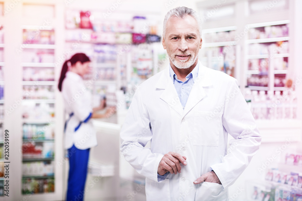 Confident grey-haired pharmacist holding his hand in the pocket