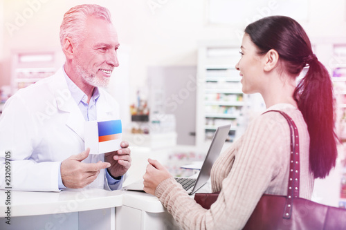 Smiling druggist revealing pills to an interested woman in a drugstore