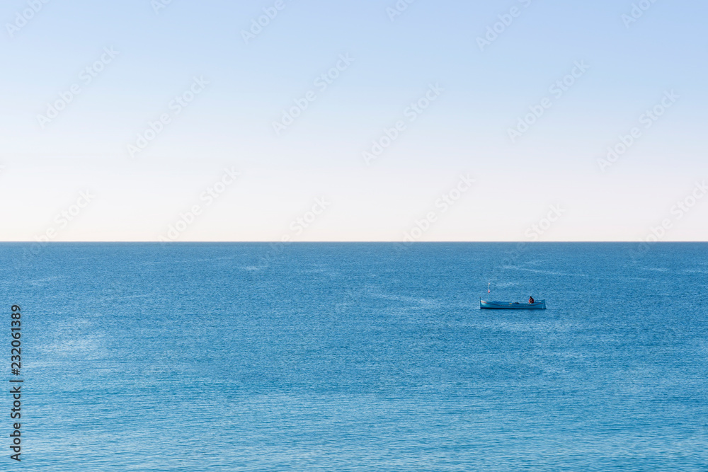 Fisherman fishing in the ocean in a small blue boat on the early morning