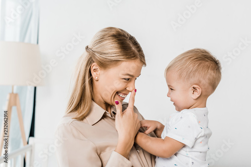 cheerful mom holding son and pointing at nose