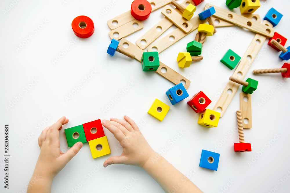 Obraz premium Close up of child hands playing with colorful wooden bricks at the table. Toddler having fun and building out of bright constructor bricks. Early learning. Top view. Flat lay.