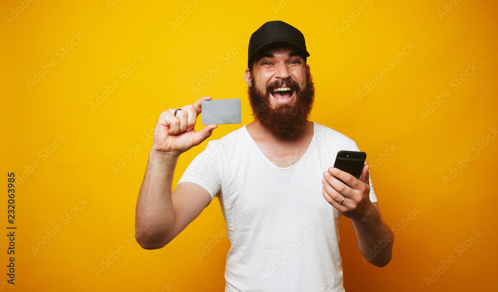 Cheerful man with beard holding credit card and smartphone Cheerful man with beard holding credit card and smartphone