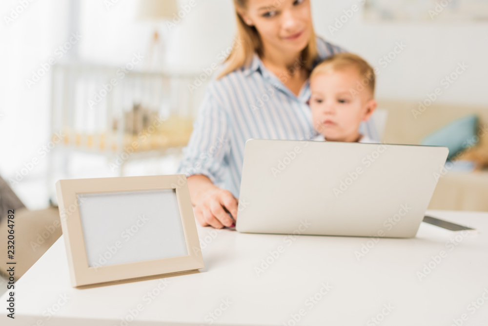 mother sitting at desk with cute toddler while using laptop, focus on foreground mother sitting at desk with cute toddler while using laptop, focus on foreground