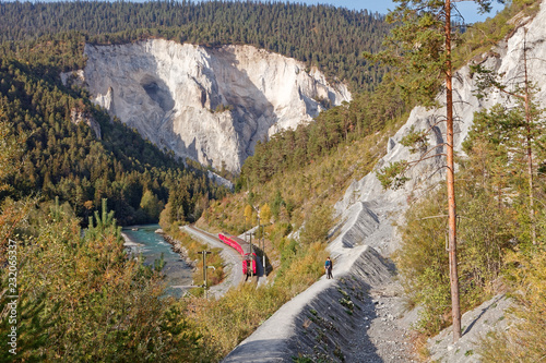 Tourists approaching Isla and observing passing by Glacier Express train in sunny autumnal Ruinaulta - Rheinschlucht (Rhine canyon), Valendas-Carrera, Switzerland photo