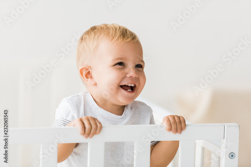 cheerful toddler standing in baby crib on white background photo