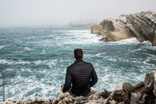 Man thinking while sitting on a rock and watching the ocean