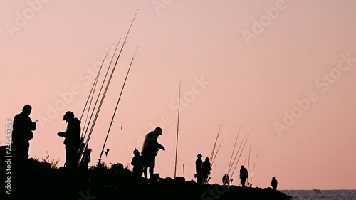 Group of fishermen standing on the bay, preparing their fishing rods. Sun is setting. photo