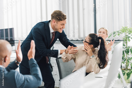 cheerful young business people greeting happy female colleague at workplace