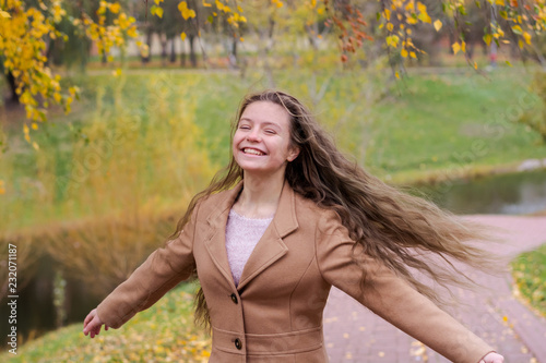 A teenager girl is spinning under foliage of a birch in the autumn park