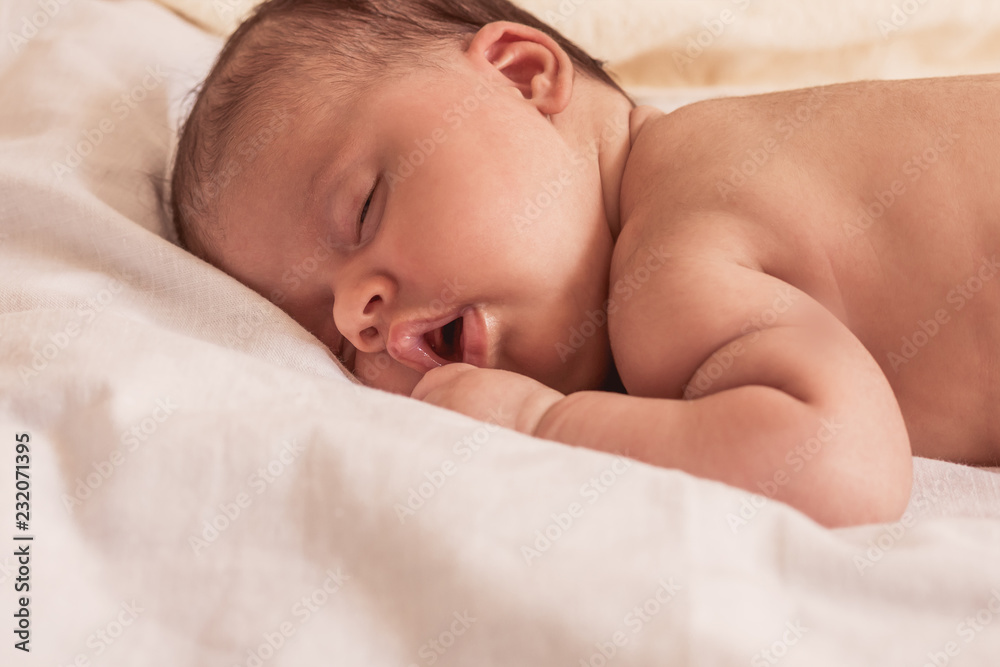 A sweet newborn infant girl is sleeping peacefully on white bedspread A sweet newborn infant girl is sleeping peacefully on white bedspread