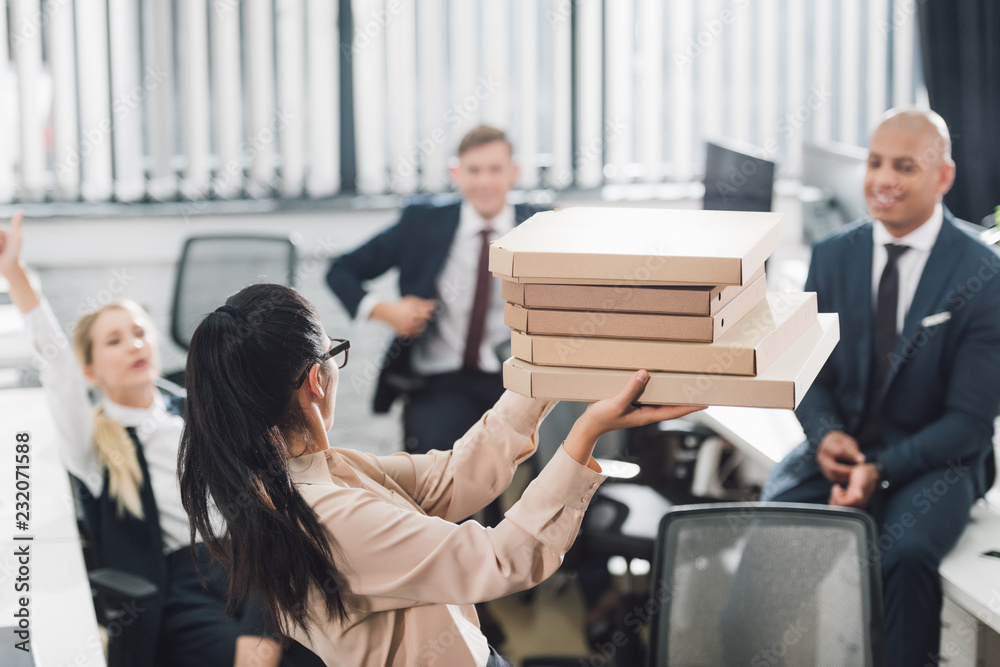 young businesswoman showing pizza boxes to happy colleagues in open space office