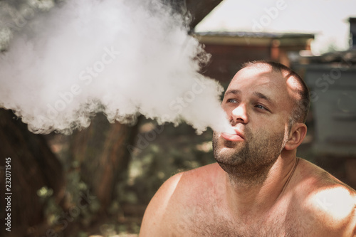 Vape man. Young man Without clothing is smoking an electronic cigarette at the summer park.