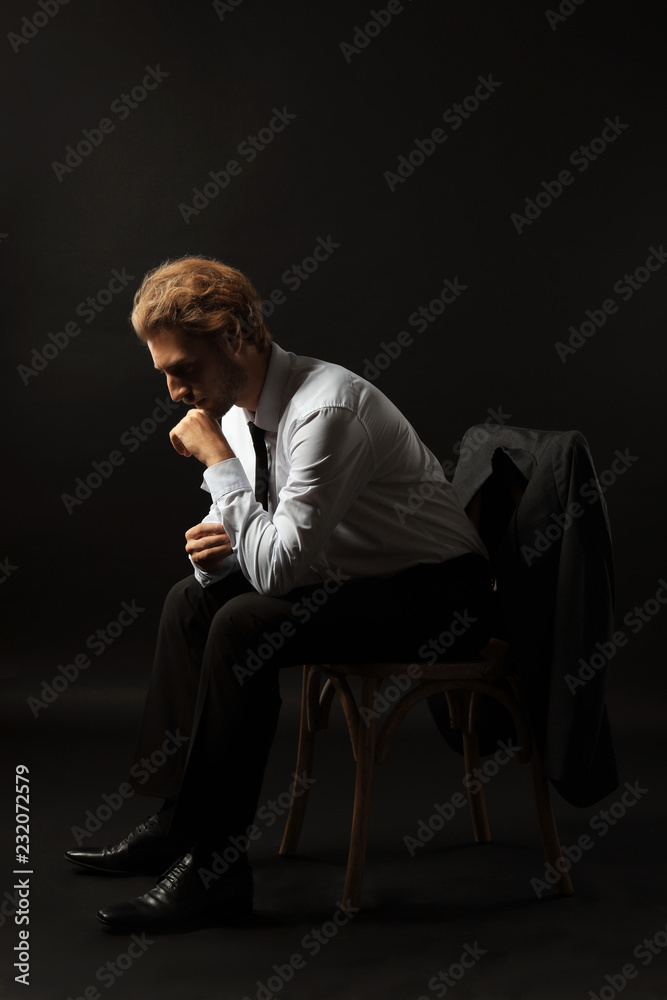 Thoughtful businessman sitting on chair against black background Thoughtful businessman sitting on chair against black background