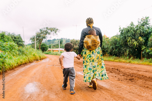 african mother and two children walk alone in red clay road in  village as a family in traditional dress photo