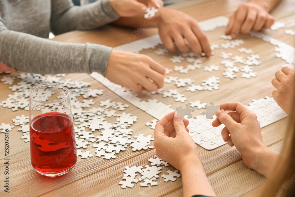 Group of people assembling puzzle on wooden table Group of people assembling puzzle on wooden table