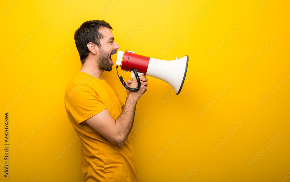Man on isolated vibrant yellow color shouting through a megaphone to announce something in lateral position Man on isolated vibrant yellow color shouting through a megaphone to announce something in lateral position