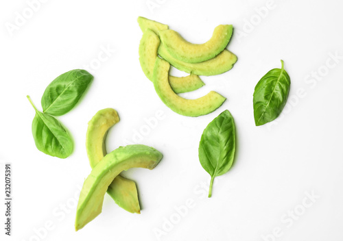 Slices of avocado and basil leaves on white background