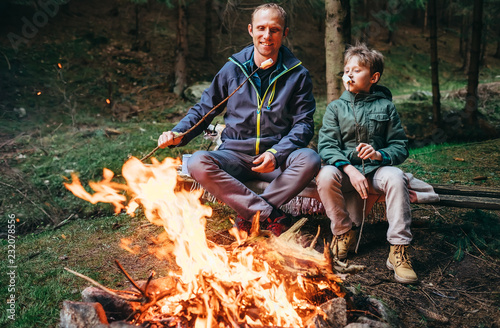Father and son roast marshmallow candies on campfire in forest
