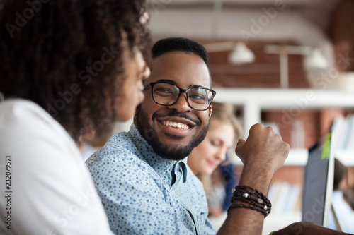 Close up of smiling African American employee look at female colleague chatting in office, happy black male worker talk with woman coworker, having casual conversation at workplace, have fun photo