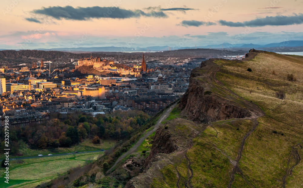 View of the Salisbury Crags from Arthur's Seat at sunrise, with the sun shining on Edinburgh's Castle in the background. Edinburgh, Scotland.  Landscape. Cityscape. Travel.