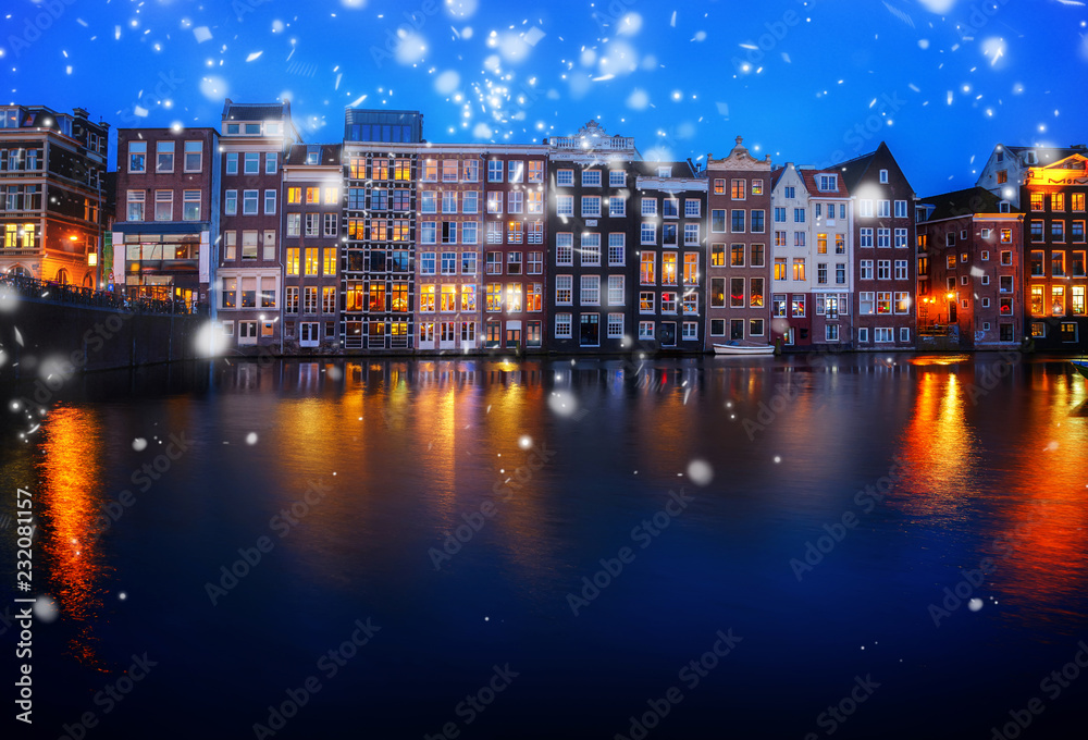 Houses facades over canal with reflections illuminated at night, Amsterdam, Netherlands with snow