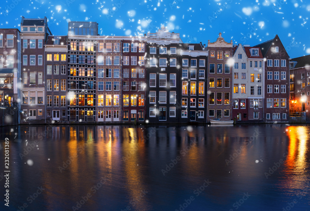 Historical houses facades over canal with reflections illuminated at night, Amsterdam with snow, Netherlands