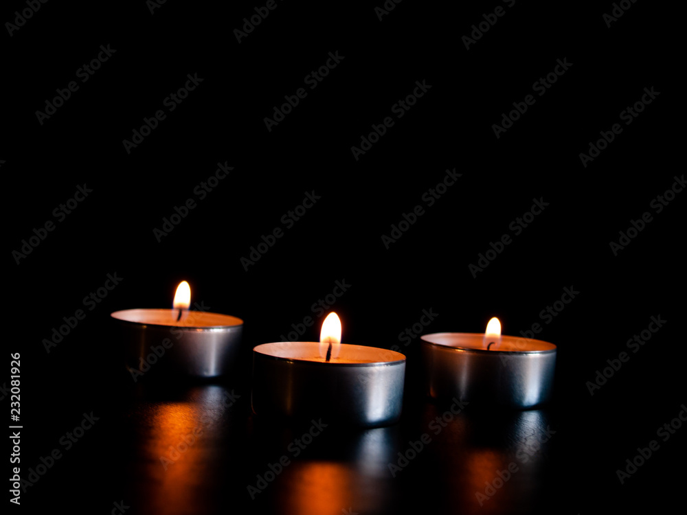 Three lighted candles with an orange flame and isolated on a black background Three lighted candles with an orange flame and isolated on a black background