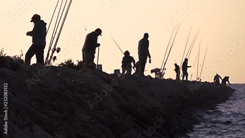 Eight fishermen standing on the coast near the lake, moving around while preparing their fishing rods. photo