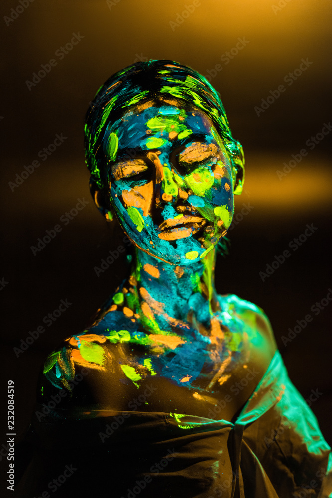 portrait of woman painted with bright neon paints on dark backdrop
