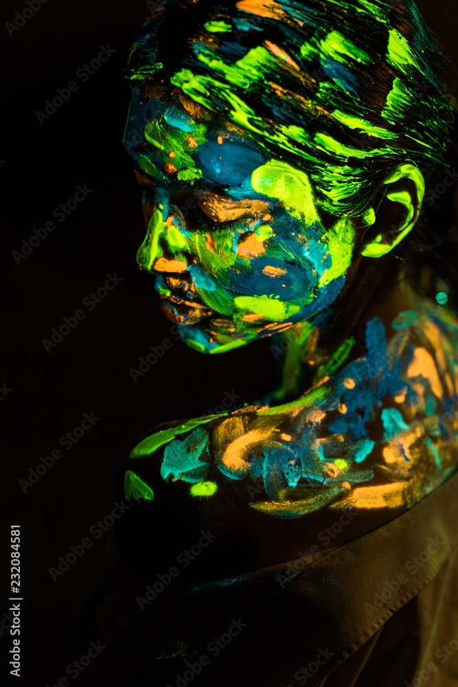 side view of woman painted with colorful ultraviolet paints on black backdrop
