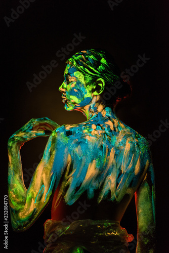 back view of model with colorful neon paints on body on black background