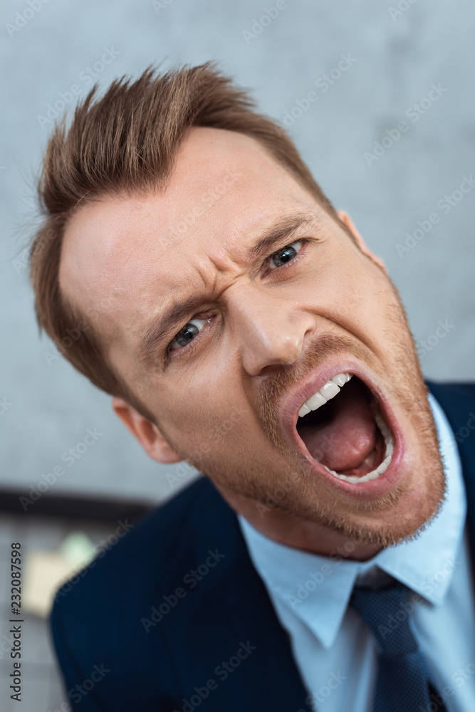 angry young businessman yelling and looking at camera in office