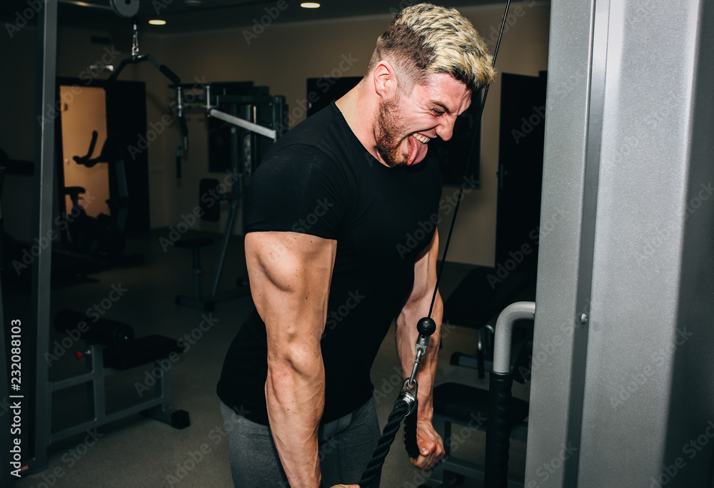 Blonde man bodybuilder is training in the gym with weights. Funny guy with  crazy emotions is doing exercises for good muscles. Fitness personal trainer  is at work. Sport motivation healthy lifestyle. Stock