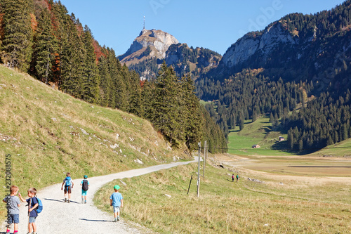 Young tourists hiking in sunny, last summer days, Appenzeller Sämtis valley with view of Hoher Kasten cable car station and aerial - Sämtis, Alpstein, Appenzell Alps, Switzerland