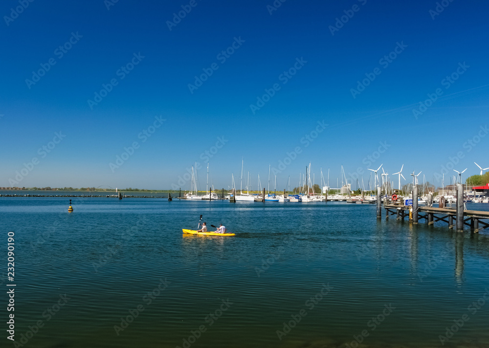 Picturesque view of two people canoeing on the sea with a bright yellow canoe at a jetty of Fehmarn island in Germany on a wonderful day with a nice blue sky. 