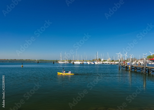 Picturesque view of two people canoeing on the sea with a bright yellow canoe at a jetty of Fehmarn island in Germany on a wonderful day with a nice blue sky. 