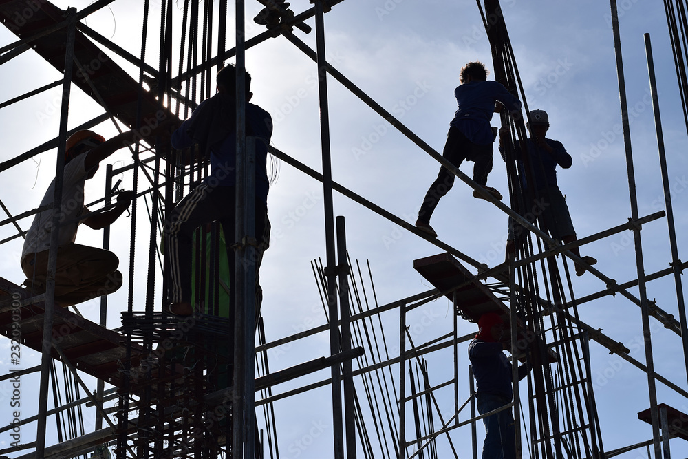 Filipino Construction steel workers assembling steel bars on high-rise building with no proper protective suits and safety shoes. underside view, silhouettes