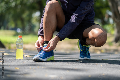 Young athlete man tying running shoes in the park outdoor, male runner ready for jogging on the road outside, asian Fitness walking and exercise on footpath in morning. wellness and sport concepts