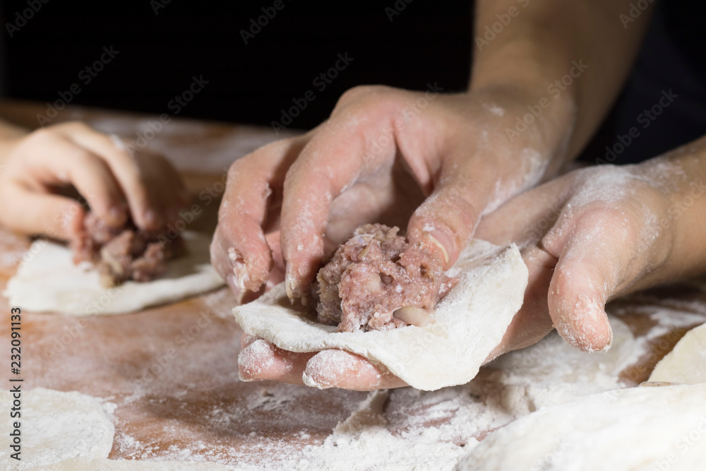 children and adults hands put minced meat in the dough, cooking meat pies