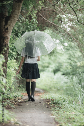 Portrait of Asian school girl walking with umbrella at nature walkway on raining