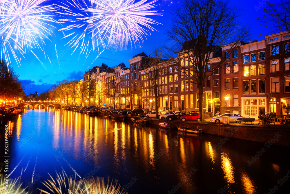 Houses over canal with lights and reflections at night with fireworks, Amsterdam, Netherlands,