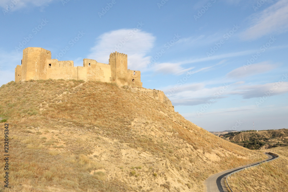 A landscape of the medieval abandoned Montearagon castle, placed over a hill among tilled crop fields, in a summer afternoon, in Aragon region, Spain